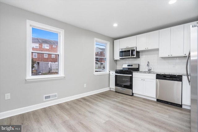 kitchen with sink, light wood-type flooring, appliances with stainless steel finishes, decorative backsplash, and white cabinets