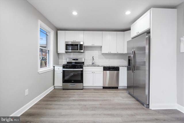 kitchen with sink, appliances with stainless steel finishes, white cabinetry, backsplash, and light stone countertops