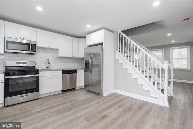 kitchen featuring white cabinetry, stainless steel appliances, light hardwood / wood-style floors, and light stone counters