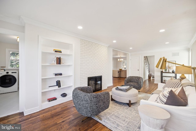 living room featuring crown molding, dark wood-type flooring, built in features, a brick fireplace, and washer / clothes dryer