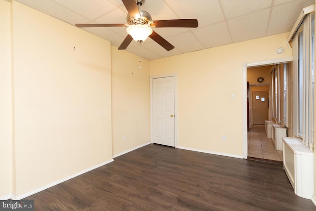 empty room featuring a drop ceiling, dark wood-type flooring, and ceiling fan