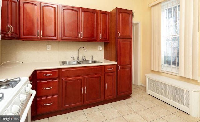 kitchen featuring sink, gas range gas stove, tasteful backsplash, light tile patterned floors, and radiator heating unit