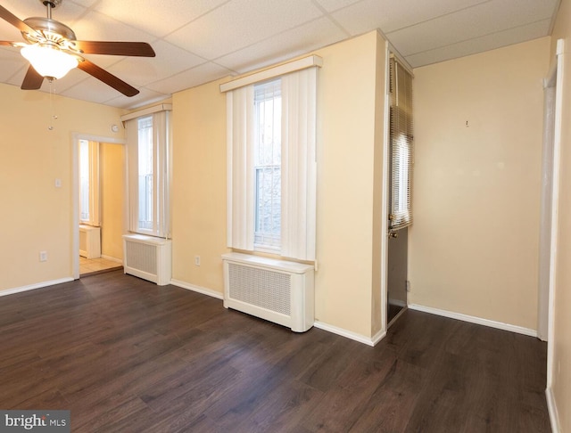 unfurnished room with a drop ceiling, dark wood-type flooring, radiator heating unit, and ceiling fan