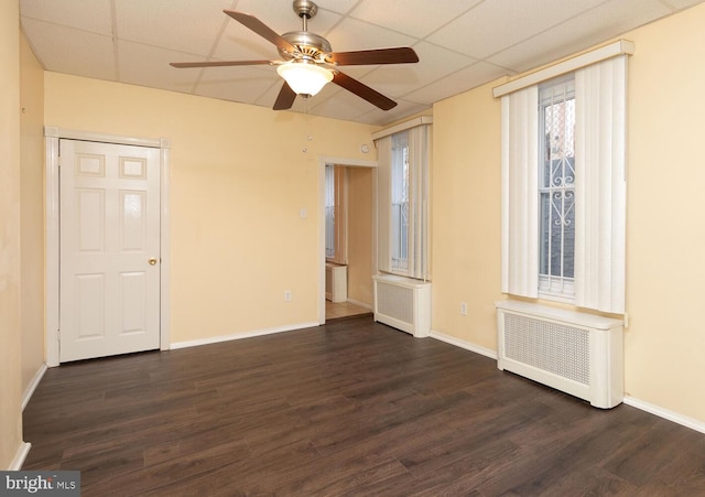 unfurnished room featuring dark hardwood / wood-style flooring, radiator heating unit, ceiling fan, and a paneled ceiling