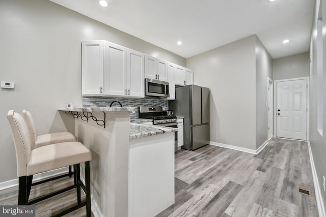 kitchen featuring a breakfast bar area, white cabinets, light stone counters, kitchen peninsula, and stainless steel appliances