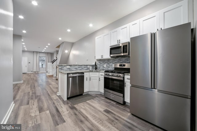 kitchen with light hardwood / wood-style flooring, appliances with stainless steel finishes, backsplash, light stone counters, and white cabinets