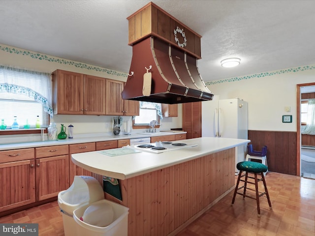 kitchen with white appliances, a kitchen breakfast bar, a center island, a textured ceiling, and light parquet flooring