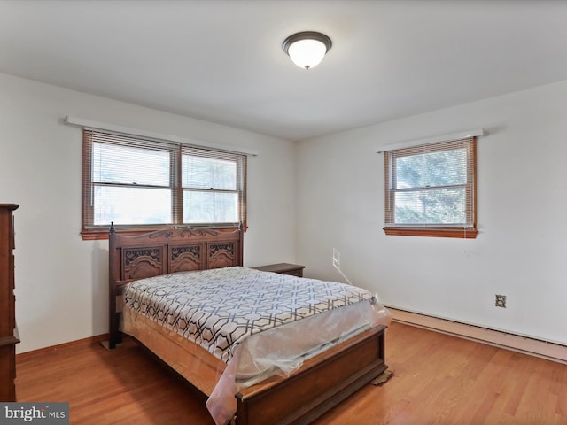 bedroom featuring hardwood / wood-style flooring, a baseboard heating unit, and multiple windows