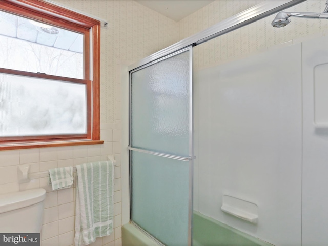 bathroom featuring tile walls, bath / shower combo with glass door, and toilet