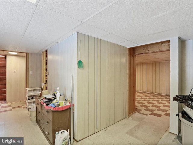 basement featuring a drop ceiling and wooden walls