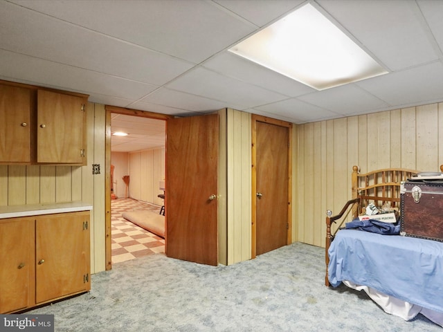 bedroom featuring light carpet, a drop ceiling, and wood walls