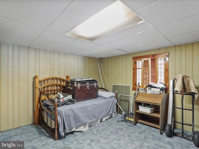 bedroom with carpet flooring, a drop ceiling, and wooden walls