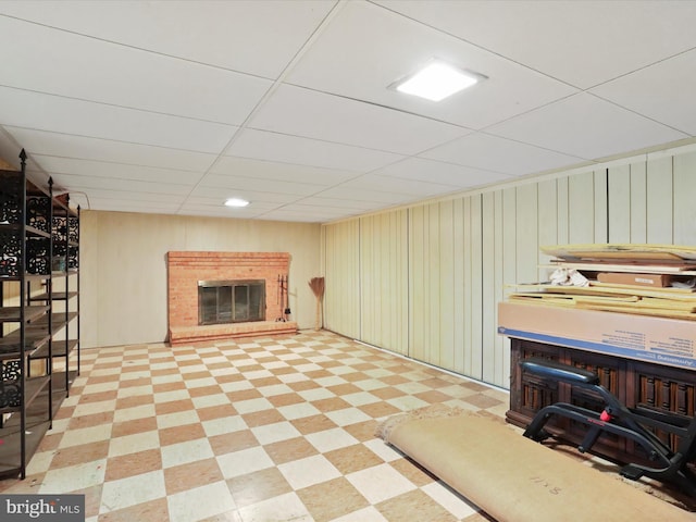 basement featuring a brick fireplace, a paneled ceiling, and wooden walls