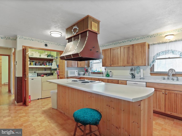 kitchen featuring sink, white appliances, a breakfast bar area, washing machine and clothes dryer, and a kitchen island