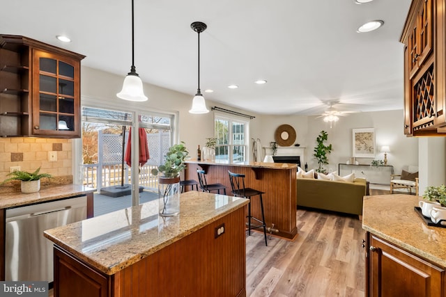 kitchen with a kitchen island, pendant lighting, dishwasher, light stone counters, and light hardwood / wood-style flooring