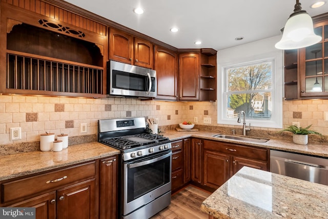 kitchen featuring sink, hanging light fixtures, light hardwood / wood-style flooring, stainless steel appliances, and light stone countertops