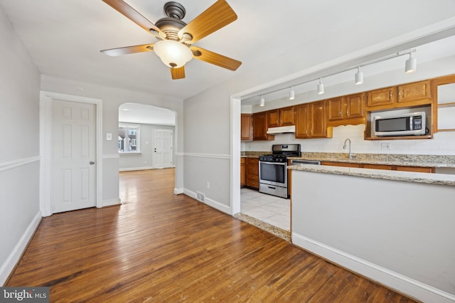 kitchen featuring sink, ceiling fan, stainless steel appliances, light hardwood / wood-style floors, and decorative backsplash