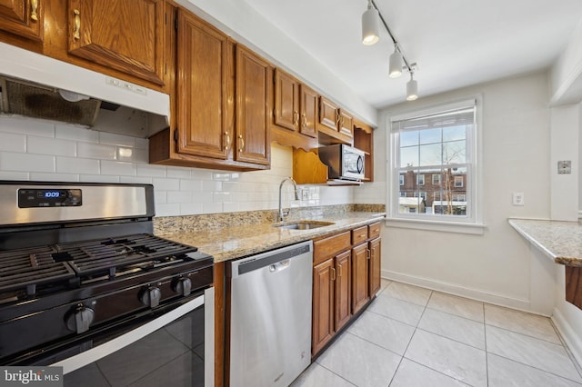 kitchen featuring sink, tasteful backsplash, light tile patterned floors, appliances with stainless steel finishes, and light stone countertops