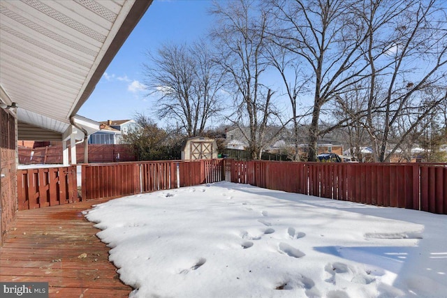 yard covered in snow with a wooden deck and a storage unit