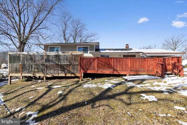 snow covered rear of property with a deck and a lawn