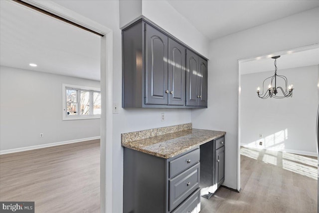 kitchen with hardwood / wood-style flooring, gray cabinets, stone counters, and a chandelier