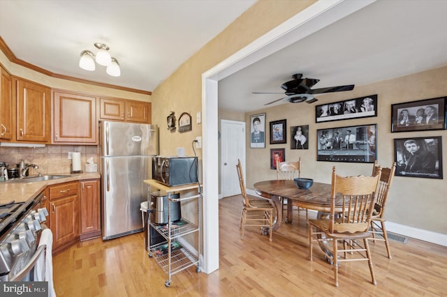 kitchen featuring appliances with stainless steel finishes, sink, decorative backsplash, ceiling fan, and light wood-type flooring