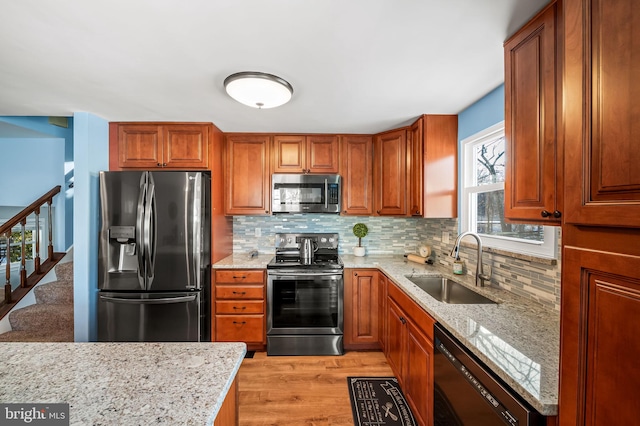 kitchen featuring sink, tasteful backsplash, light stone counters, light hardwood / wood-style flooring, and stainless steel appliances