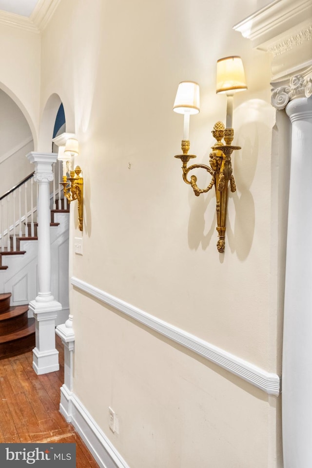 hallway featuring wood finished floors, baseboards, ornamental molding, stairway, and ornate columns