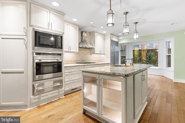 kitchen with a warming drawer, backsplash, a sink, wall chimney range hood, and built in appliances