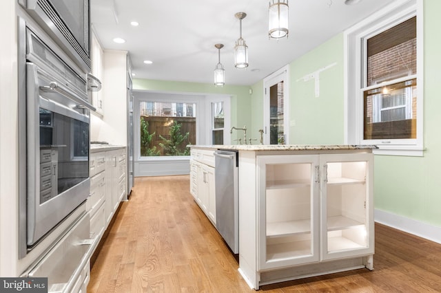 kitchen featuring stainless steel appliances, pendant lighting, white cabinets, and light wood-style flooring