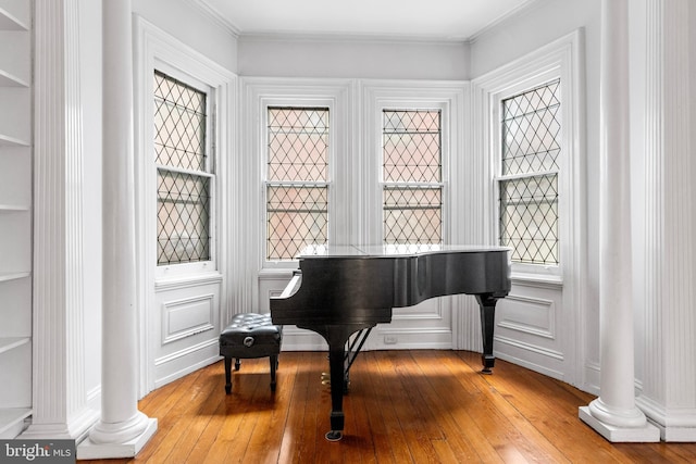 sitting room with decorative columns, a decorative wall, ornamental molding, light wood-type flooring, and plenty of natural light