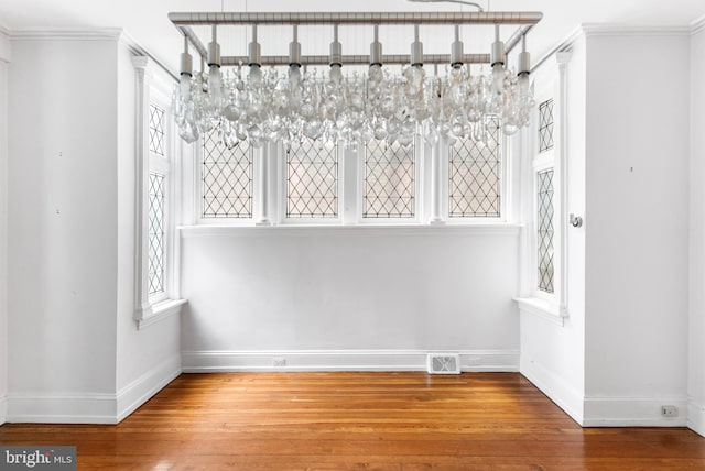 unfurnished dining area with ornamental molding, wood finished floors, visible vents, and baseboards