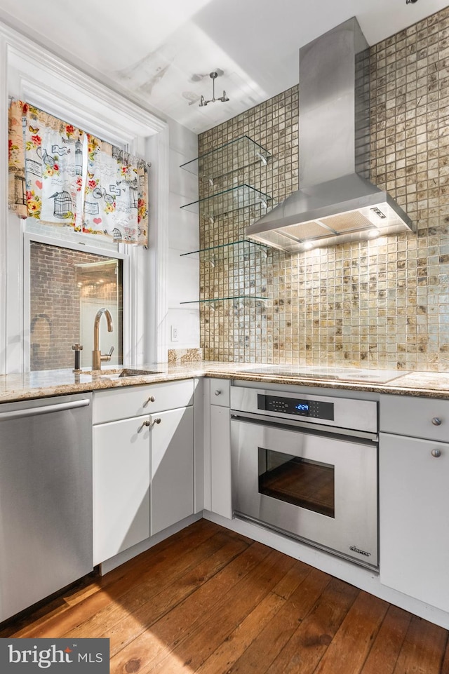 kitchen with wall chimney range hood, backsplash, stainless steel appliances, and dark wood-type flooring