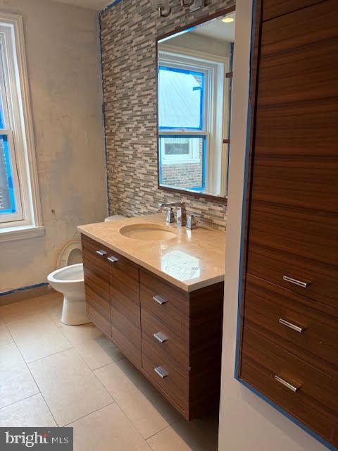 bathroom featuring toilet, tile patterned flooring, backsplash, and vanity