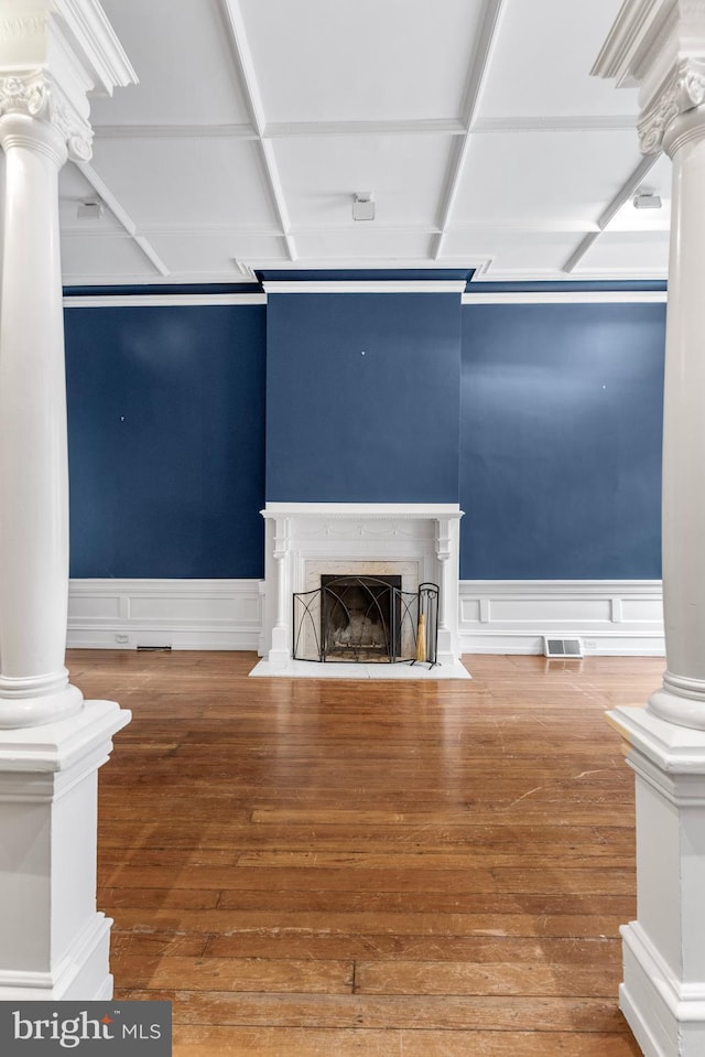 unfurnished living room featuring ornate columns, visible vents, a fireplace with flush hearth, wainscoting, and hardwood / wood-style floors