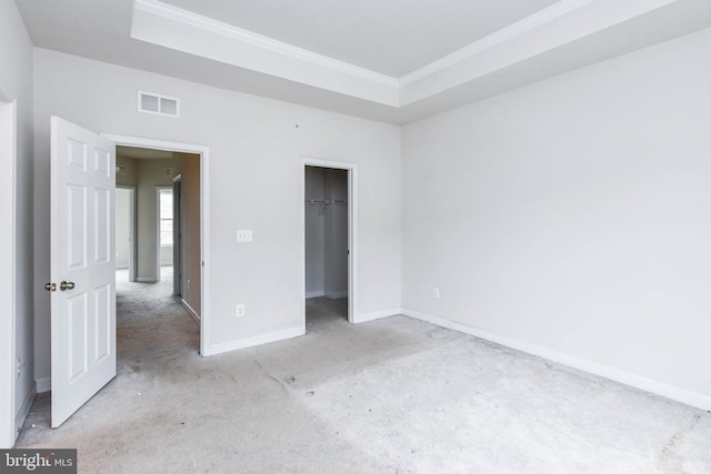 unfurnished bedroom with crown molding, a tray ceiling, a closet, and a spacious closet