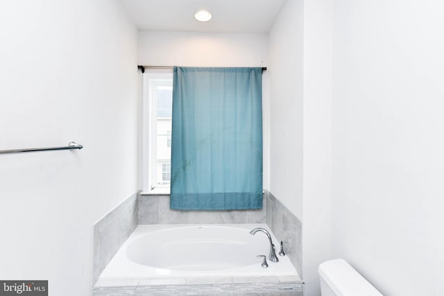 bathroom with toilet and tiled tub