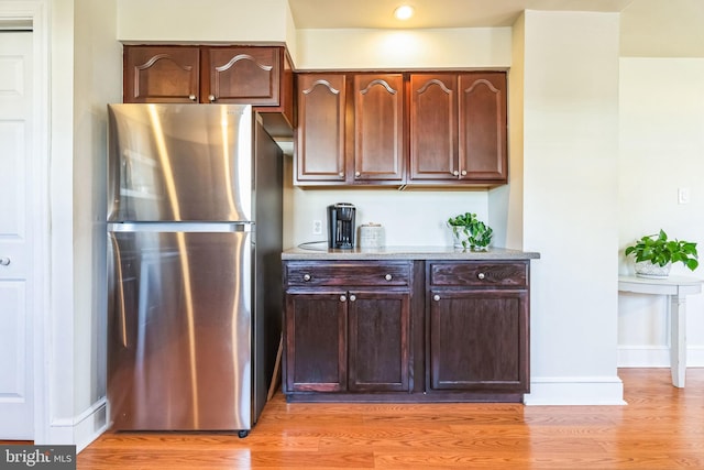 kitchen featuring dark brown cabinets, stainless steel fridge, and light wood-type flooring