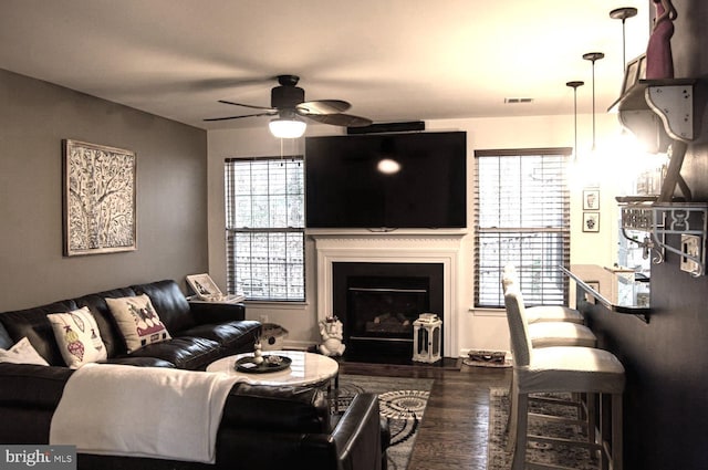 living area with a wealth of natural light, a fireplace, a ceiling fan, and wood finished floors