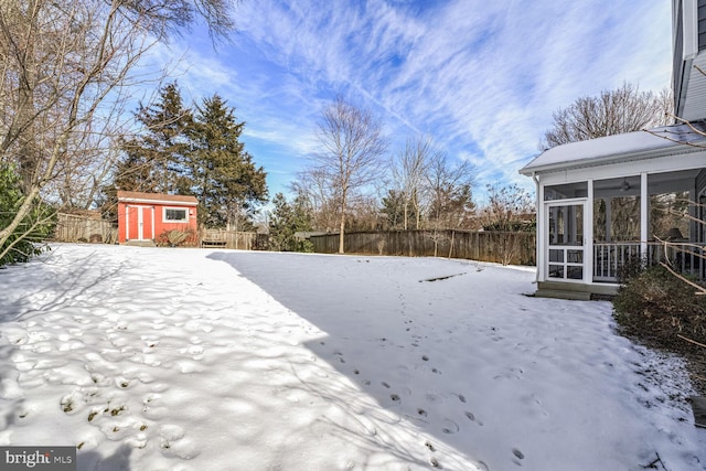 yard covered in snow with a fenced backyard, a shed, an outdoor structure, and a sunroom