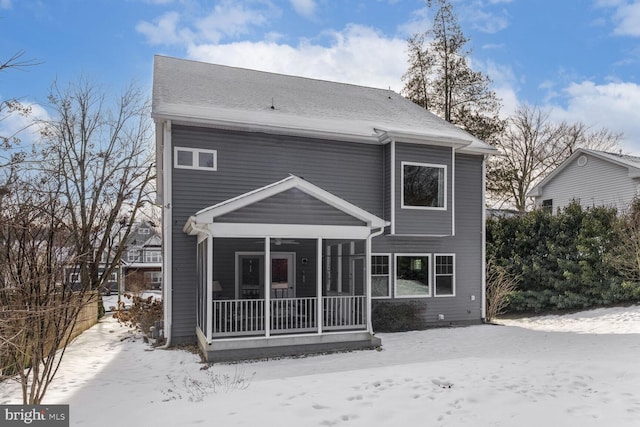 snow covered rear of property with a sunroom