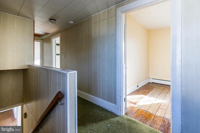 hall featuring hardwood / wood-style floors, wood walls, and baseboard heating