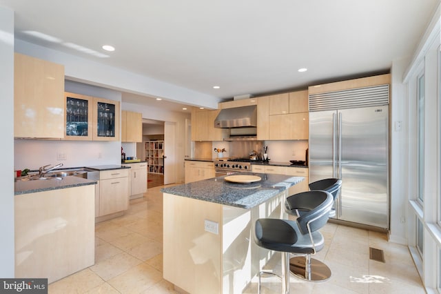 kitchen featuring wall chimney range hood, light brown cabinetry, a kitchen island, and premium appliances