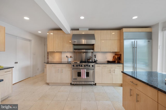 kitchen featuring ventilation hood, dark stone countertops, light brown cabinetry, and premium appliances