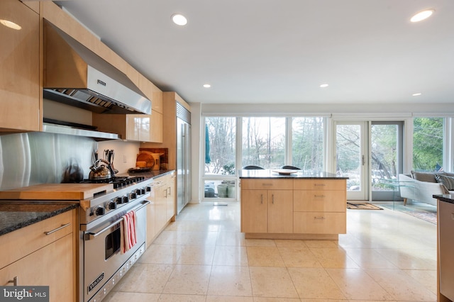 kitchen featuring premium appliances, light tile patterned flooring, exhaust hood, dark stone counters, and light brown cabinets