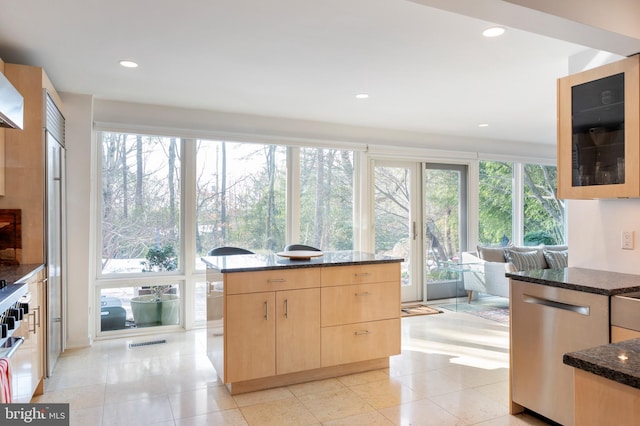 kitchen featuring light brown cabinetry, light tile patterned floors, stainless steel dishwasher, and dark stone counters