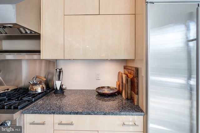 kitchen with stainless steel appliances, light brown cabinetry, and dark stone counters