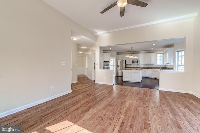 kitchen with white cabinetry, wood-type flooring, decorative light fixtures, appliances with stainless steel finishes, and ceiling fan with notable chandelier