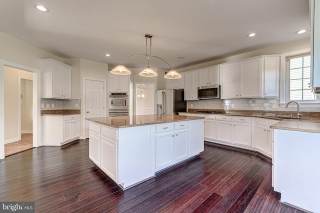 kitchen with pendant lighting, appliances with stainless steel finishes, white cabinetry, dark hardwood / wood-style floors, and a kitchen island