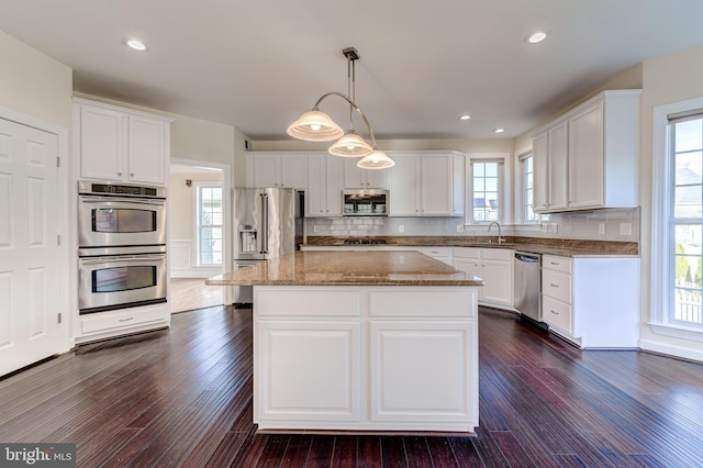 kitchen featuring appliances with stainless steel finishes, hanging light fixtures, a kitchen island, and white cabinets